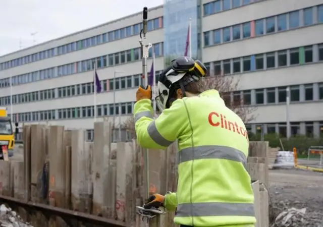 En mätningsingenjör från Clinton Mätkonsult som genomför utstakning och lägeskontroll på en byggarbetsplats, där projekterade detaljer överförs till marken för att säkerställa att byggnader placeras korrekt enligt bygglov och ritningar.